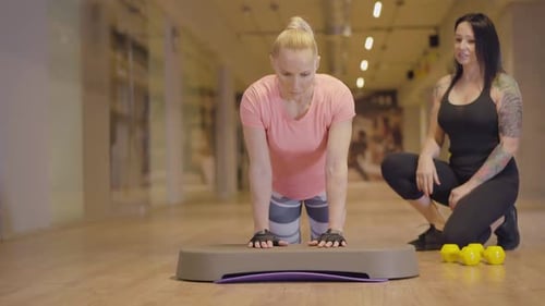 Professional Personal Trainer Controls Workout of Athletic Woman in Gym. Tatooed Caucasian Woman