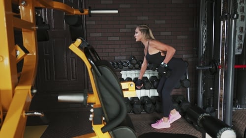 Fitness Woman Performs Bent-over Dumbbell Row Exercise in the Gym