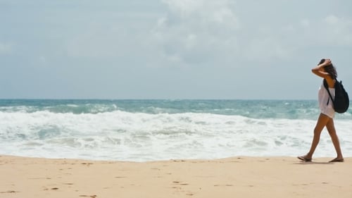 a Young Woman with a Backpack Walking Along a Deserted Beach