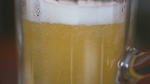 Auf dem Tisch steht ein leeres Glas, in das Bier mit einem Schaum gegossen wird