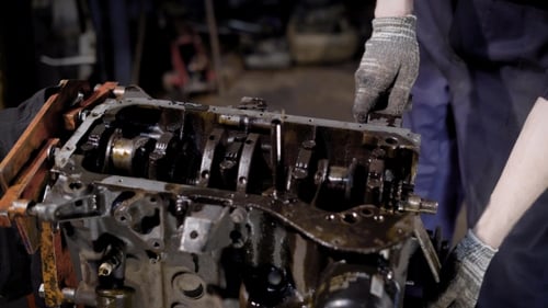 Crop Repairman Standing and Servicing Oily Engine in Workshop