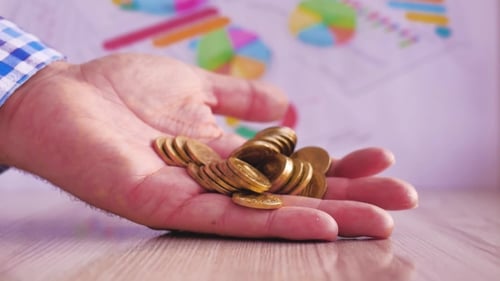 Hand Drops Pile of Gold Coins on Table