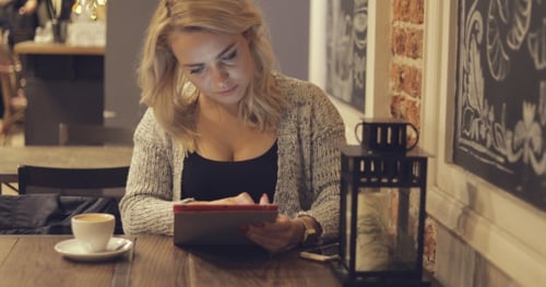 Woman Using Tablet and Drinking Coffee at Cafe