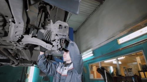 Auto Mechanic Working on Lift Repairing Vehicle
