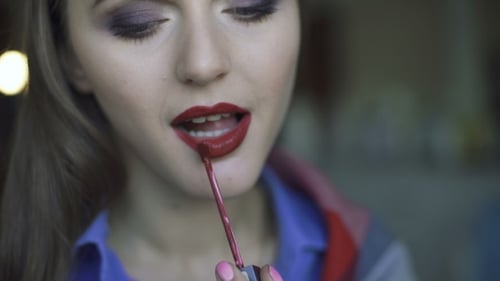 Junge schöne Frau, die ihren Bordo-Lippenstift auf einen Spiegel aufträgt