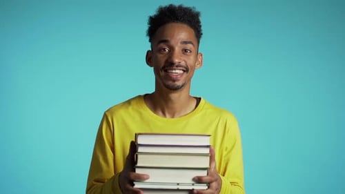 African Student on Blue Background in The Studio Holds Stack of University Books