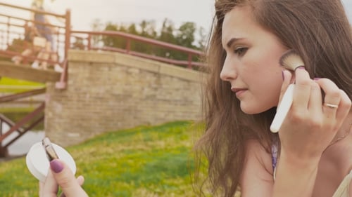 Young Beautiful and Well-groomed Girl with Long Hair in a Park in Nature. She Uses Powder To Powder