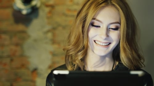 A Young Lady Smiling, Enjoying Tablet in Cafe