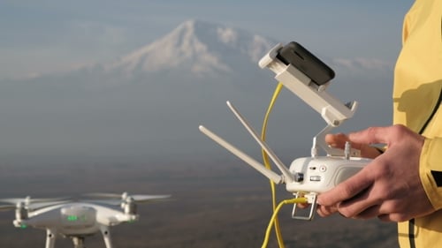 Man Hands Control Flying Quadcopter near Mountain
