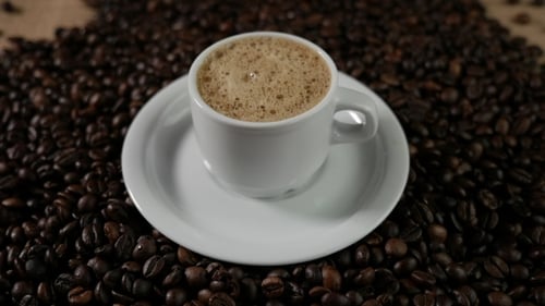 Eine weiße Tasse verdampfenden Kaffeeschaum auf einem Tisch mit gebratenen Bohnen