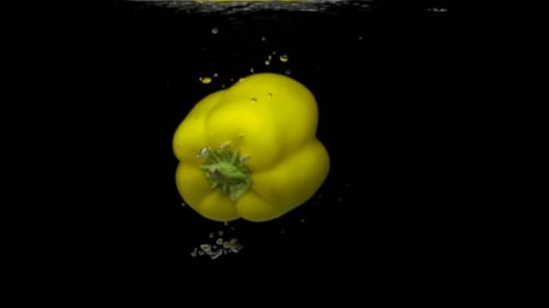Frischer grüner Paprika spritzt im Wasser auf schwarzem Hintergrund