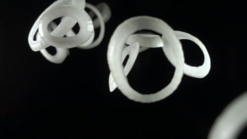 White Onion Rings Falling on a Black Background