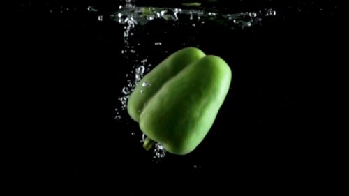 Frischer grüner Paprika spritzt im Wasser auf schwarzem Hintergrund
