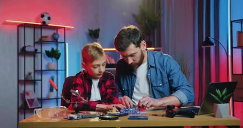 Padre ayudando a ensamblar las pequeñas piezas de Constructor junto con su agradable e interesado hijo adolescente