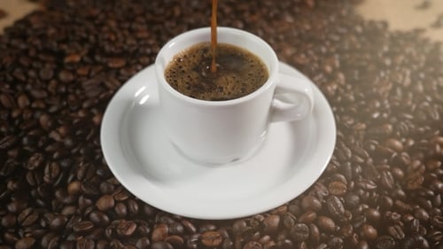 White Cup of Evaporating Coffee on the Table with Roasted Beans