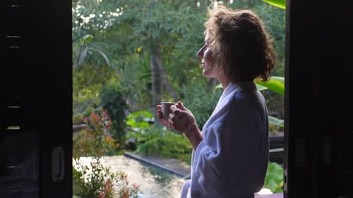 Woman in Robe Drinks Coffee in Tropical Setting