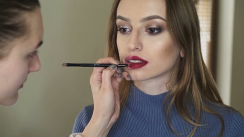 Maskenbildnerin trägt Lippenstift auf die Lippen von Mädchen auf