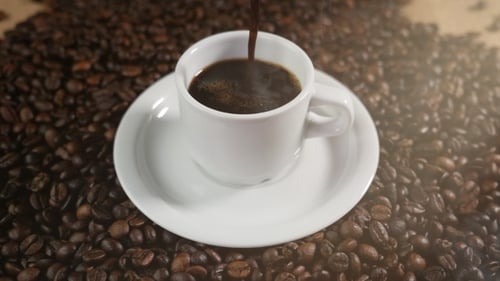 Fresh Coffee Poured Into Cup on Coffee Beans