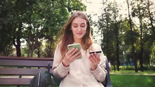 Woman Using Phone and Credit Card on Park Bench