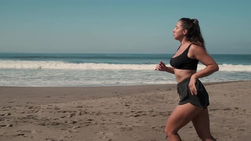 Woman Running on Sandy Beach Next to Ocean Waves