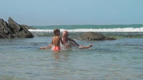 Cute Boy and Father Play in Clean Ocean Water Against Waves