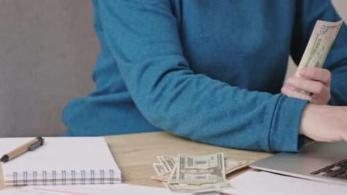 Adult Counting Money at Desk with Laptop