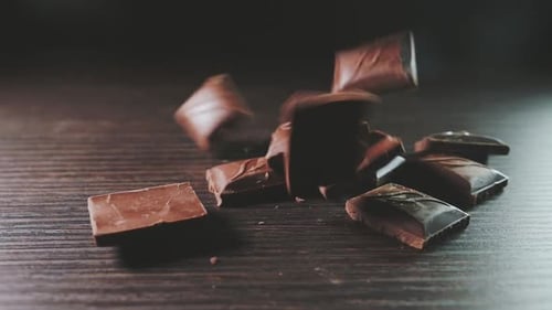 Falling Blocks of Dark Chocolate on Wooden Table