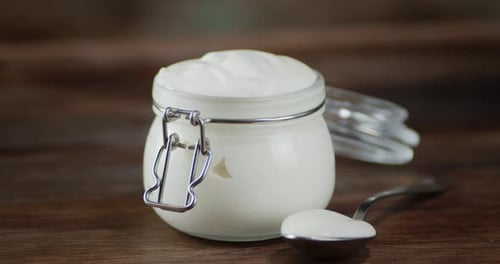 Le bocal en verre avec de la crème sure tourne lentement sur la table.
