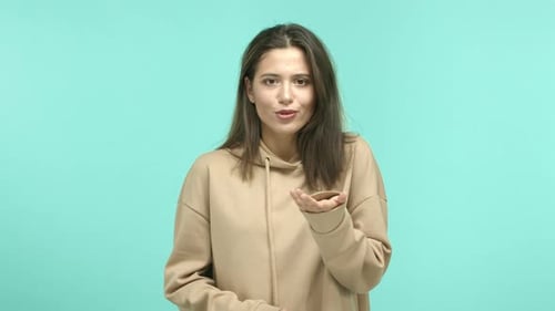Schönes weibliches Model mit dunklem Haar und beigem Hoodie, der in die Kamera zeigt, dann fange an, das Angebot abzulehnen