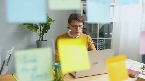 Gut aussehender Typ, der im Büroraum mit Computer hinter einer Glaswand arbeitet