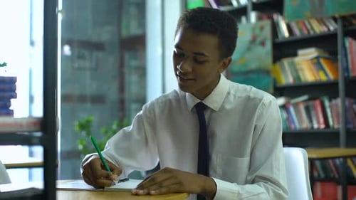 Teen Student Writing in Library Notebook