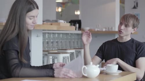 Young Successful Guy and Girl Communicate Sitting at the Table in a Cozy Cafe or Restaurant. Friends