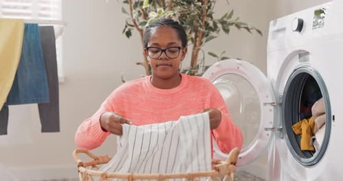 Woman in Glasses Performs Household Chores in Bathroom Laundry Room Kneels with Wicker Basket Filled