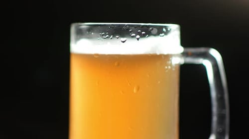 Cerveja gelada artesanal em caneca com espuma e bolhas de ar girando isoladas no fundo preto do estúdio