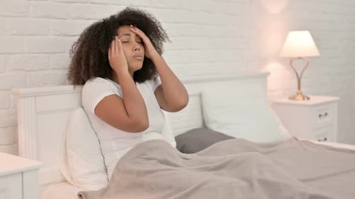Young African Woman with Headache Sitting in Bed