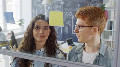 Young Colleagues Arranging Sticky Notes on Glass Wall in Office