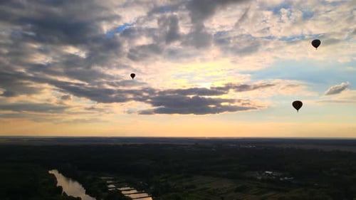 Silhouettes of Hot Air Balloons Flying Over Countryside Near Small European City at Summer Sunset in