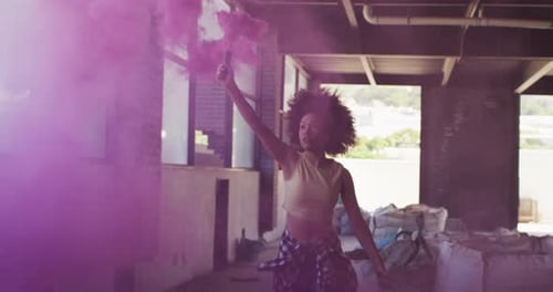 Mixed race woman holding purple flare running through an empty building
