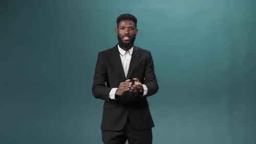 Ein afrikanischer attraktiver Mann im schwarzen Smoking steht und applaudiert in die Kamera