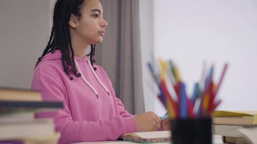 Side View of Beautiful Young African American Girl Sitting at the Table and Listening Carefully To