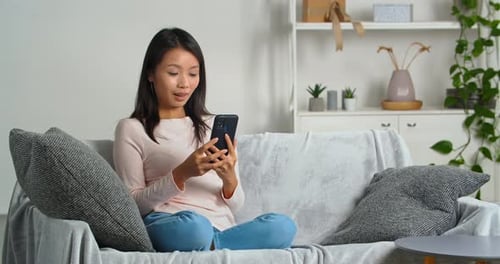 Woman Relaxing Using Smartphone on Couch Indoors