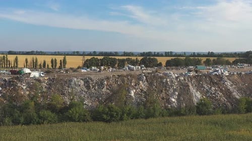 Aerial View of Rubbish Pile Lying Among Field in Rural. Flying Over Industrial Trucks Dumping Trash