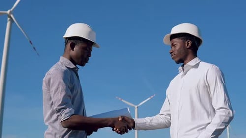 Zwei männliche afroamerikanische Elektroingenieure stehen vor dem Hintergrund einer Windmühle in der Luft