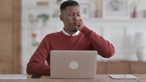 African Man Coughing while using Laptop in Office