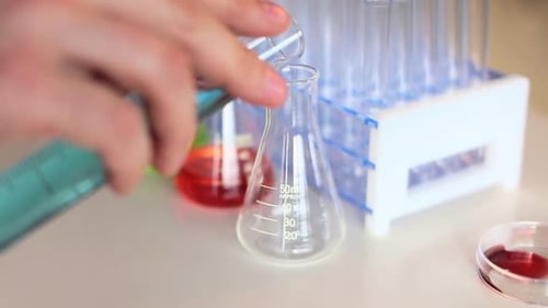 Scientist pours blue liquid into glass beaker