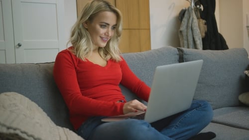 Woman Works on Laptop Sitting on Couch Indoors