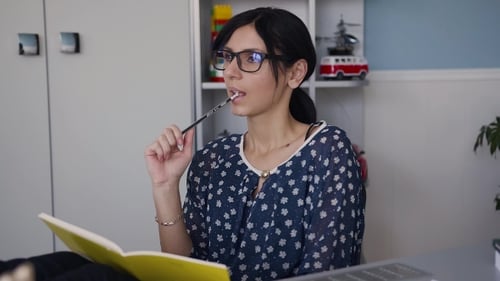 Woman Thinking and Writing in Notebook at Desk