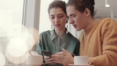 Two Young People Using Phone in Cafe