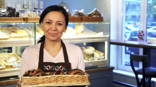 Mature Female Baker Posing at Her Store with a Basket Full of Croissants