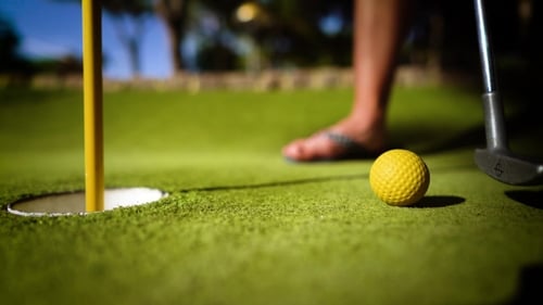 Mini Golf Yellow Ball with a Bat Near the Hole at Sunset